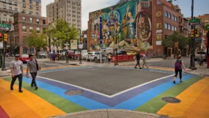 A crosswalk outlined in rainbows against a colorful background mural.