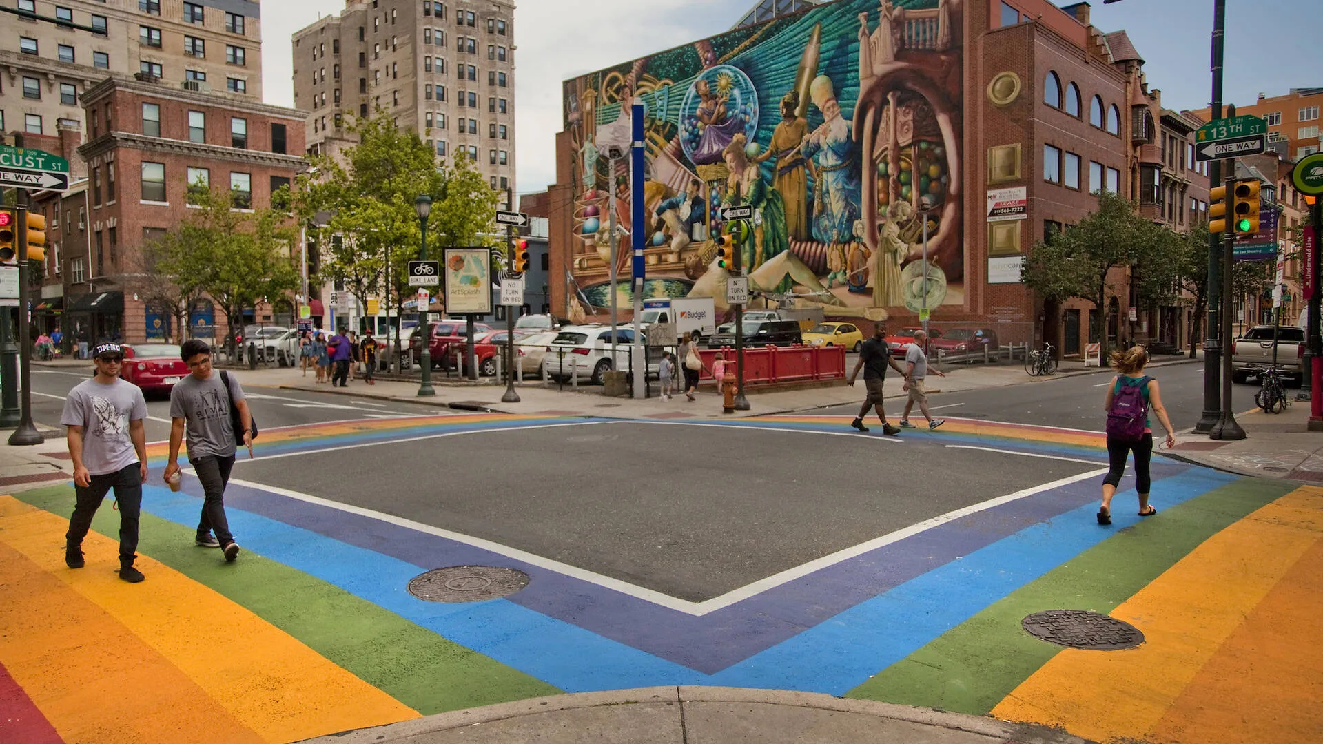 A crosswalk outlined in rainbows against a colorful background mural.
